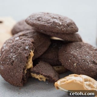 A stack of keto chocolate peanut butter cookies with a scoop of peanut butter in front