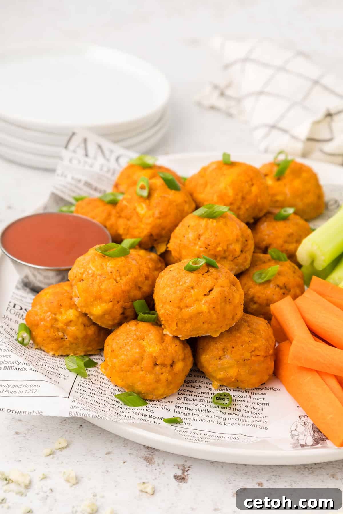 Keto Countdown Nibbles for New Year's Eve 8 Buffalo Chicken Meatballs piled up on a white plate with carrots and celery sticks.