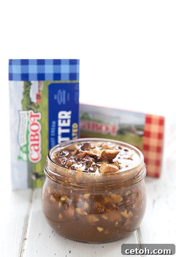 Keto Decadent Pecan Praline Sauce 6 A charming glass jar brimming with homemade Keto Praline Pecan Sauce, artfully placed on a white table with two bricks of Cabot Creamery butter in the background.