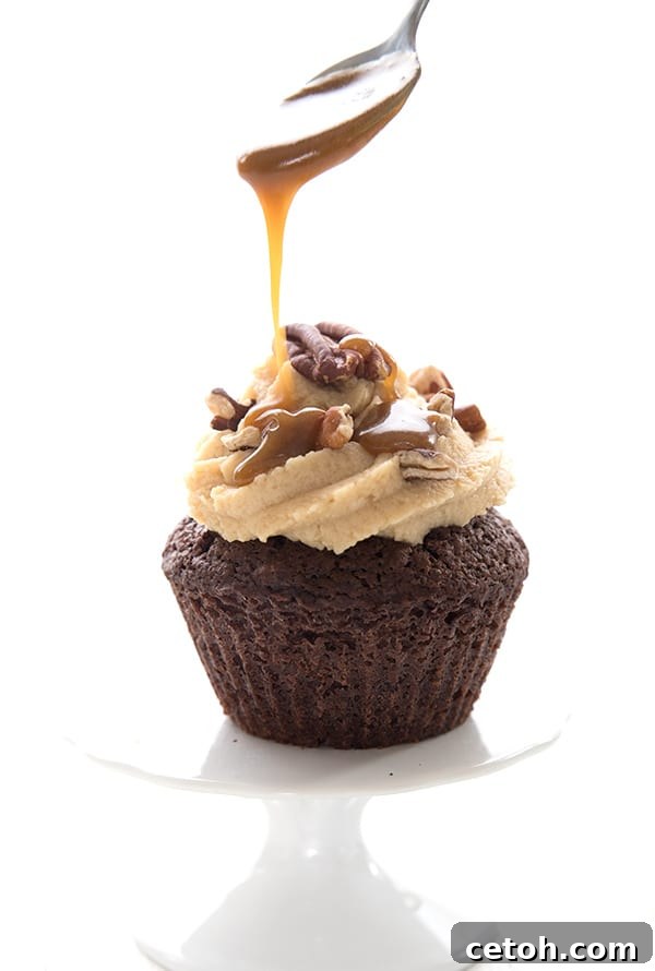 Drizzling sugar-free caramel sauce over a keto turtle cupcake on a white cake stand. 