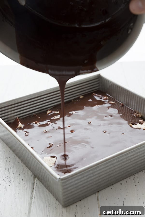 Pouring rich chocolate frosting over keto Mississippi mud bars, creating a smooth, glossy top layer.