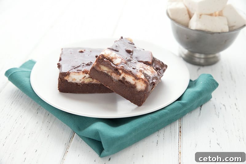 Two keto Mississippi Mud Bars on a white plate over a teal napkin, with a bowl of marshmallows in the background.