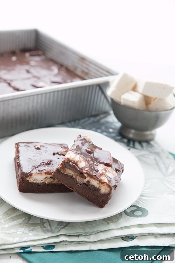 Two Mississippi Mud Bars on a white plate, with the pan of bars in the background, ready to be enjoyed.