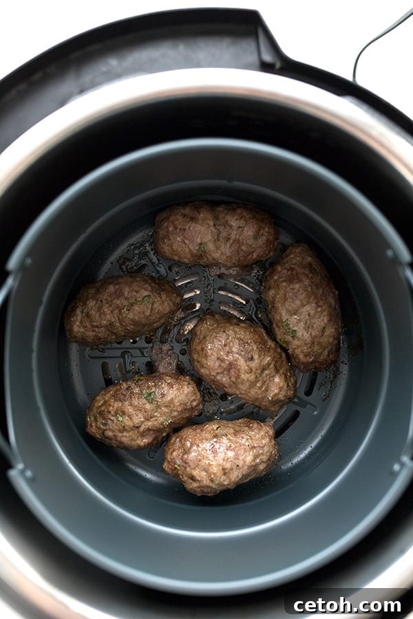 Close-up, top-down view of perfectly formed lamb kofta patties, sizzling gently inside an air fryer basket, showcasing their golden-brown crust.