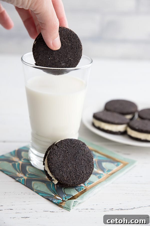 A hand dipping a keto oreo cookie into a glass of milk