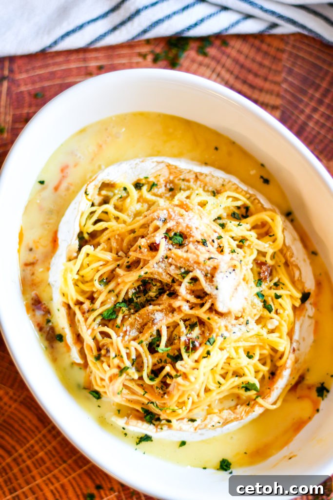 Creamy Baked Brie Spaghetti 3 A delicious serving of Baked Brie Spaghetti twirled around a fork, showing the creamy cheese sauce, pieces of sun-dried tomato, and fresh basil against a blurred background of the full dish.