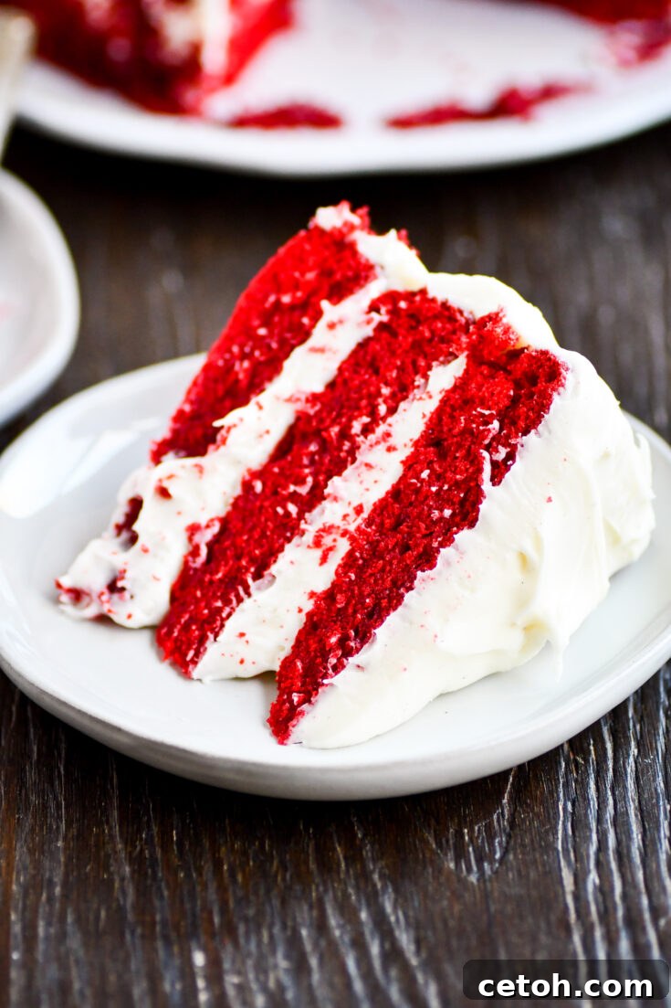 A slice of Cakeman Raven Red Velvet Cake on a white plate, showcasing its vibrant red layers and rich cream cheese frosting, ready to be enjoyed.