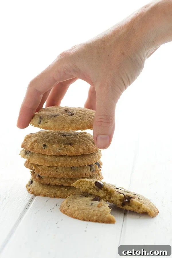 A hand gently picking up a low carb, grain-free chocolate chip cookie from a neatly stacked pile, highlighting its perfect texture.