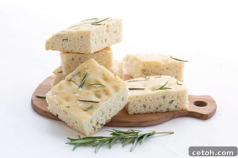 Golden-brown slices of keto focaccia bread on a small wooden cutting board, with a sprig of fresh rosemary.