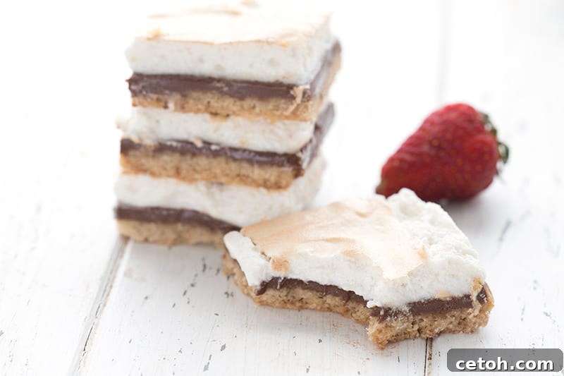 A delicious stack of keto s'mores bars on a white table, with one bar in front and a fresh strawberry.