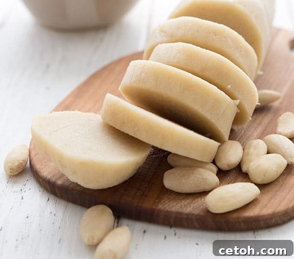 A log of beautifully shaped keto marzipan on a wooden cutting board, surrounded by blanched almonds.