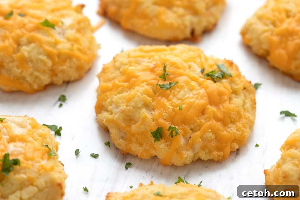Close-up shot of fluffy keto drop biscuits on a white wooden table, garnished with herbs.