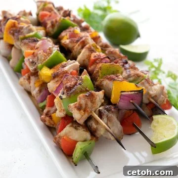 A platter full of freshly grilled keto chicken skewers, with lime and cilantro in the background.
