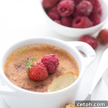 Keto Custard in a white ramekin with a spoonful taken out of it. A bowl of raspberries in the background.