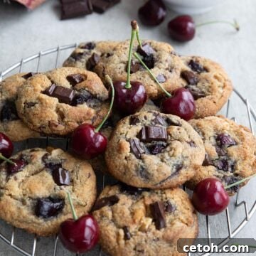 Decadent Keto Cherry Chocolate Chunk Cookies 11 Keto Cherry Chocolate Chunk Cookies on a cooling rack with a bowl of cherries in the background.