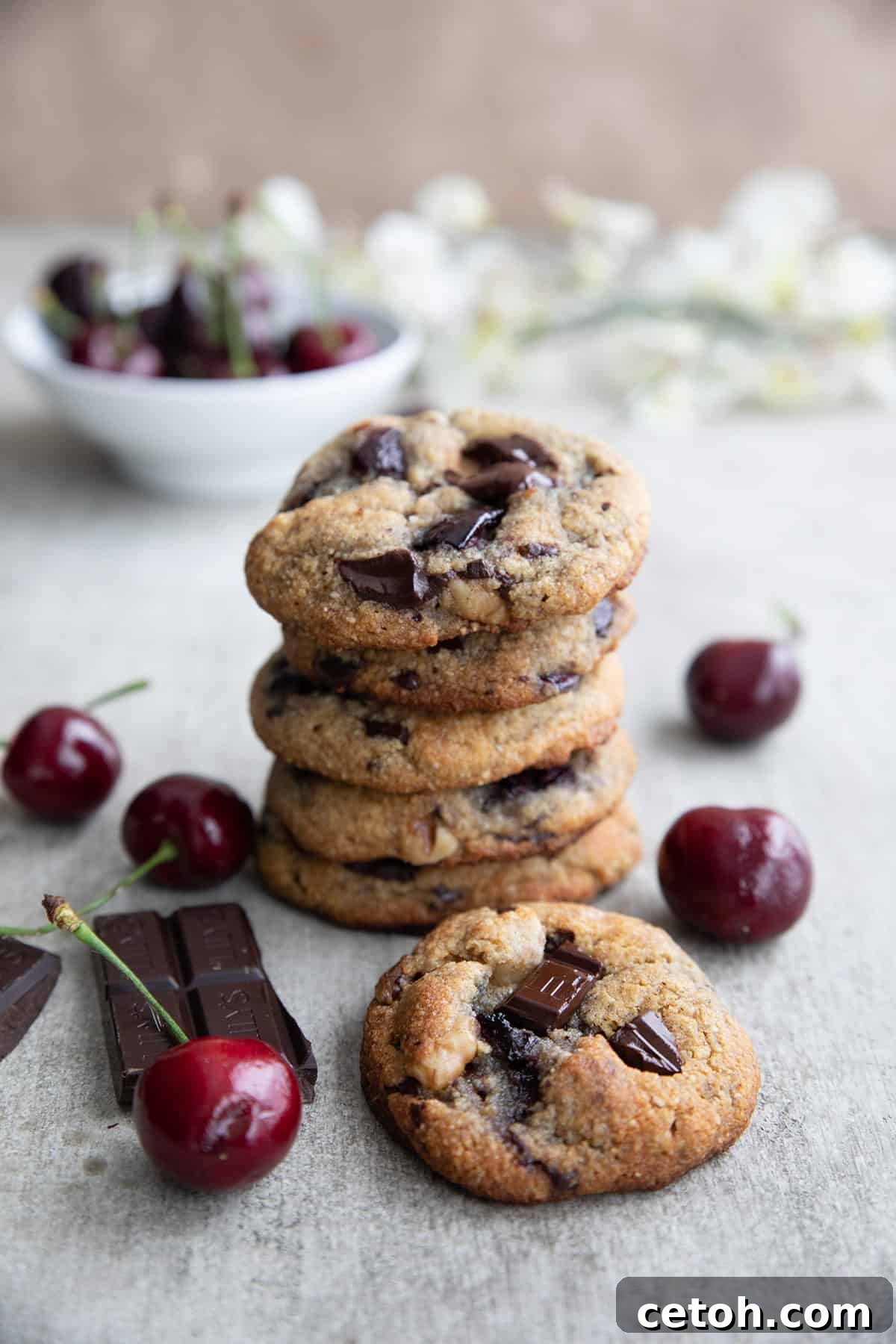 Decadent Keto Cherry Chocolate Chunk Cookies 7 A stack of Keto Cherry Chocolate Chunk Cookies on a concrete table with cherries strewn around.