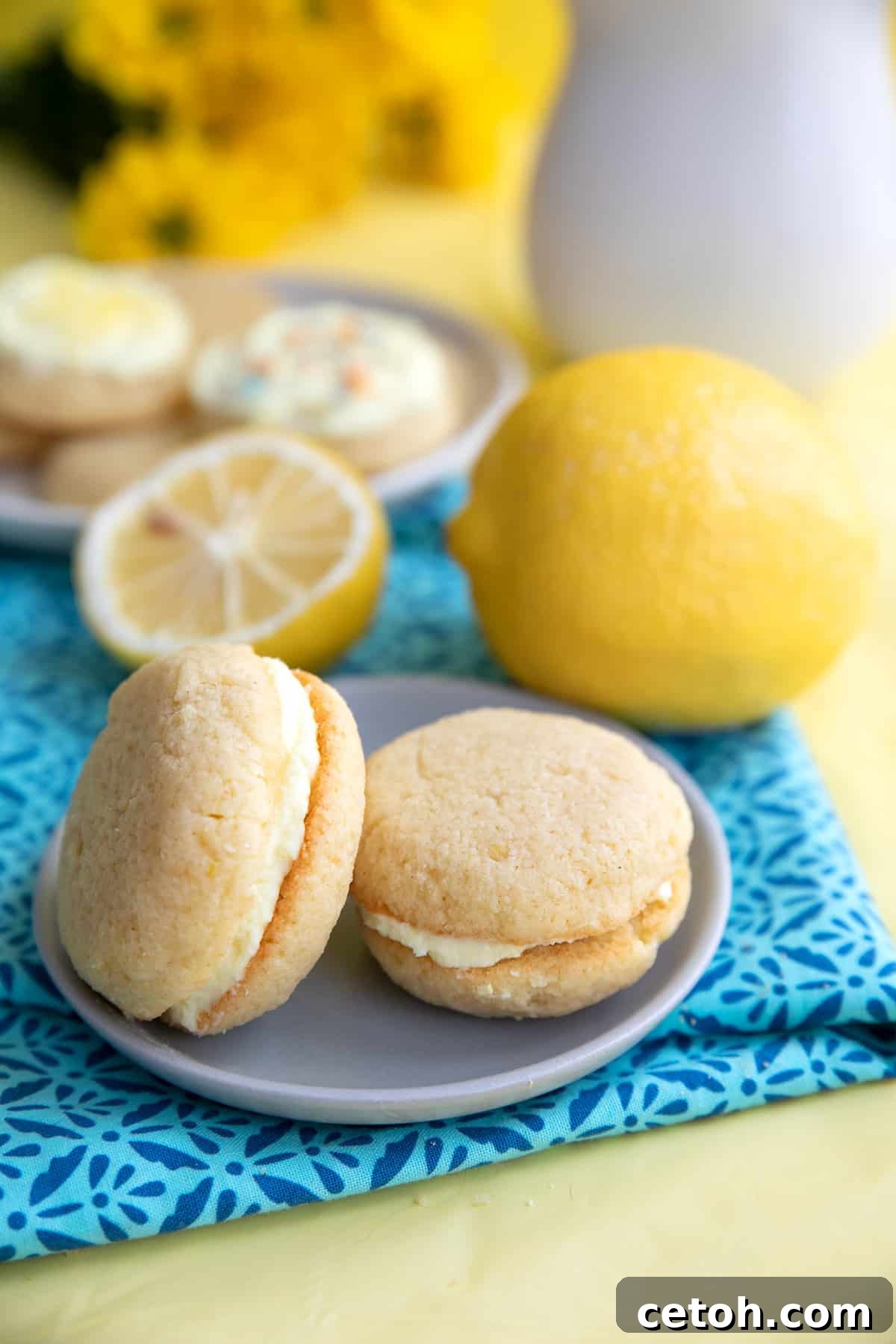 Decadent Keto Cherry Chocolate Chunk Cookies 9 Two keto lemon cookies on a small plate over a patterned blue napkin, with lemons in the background.