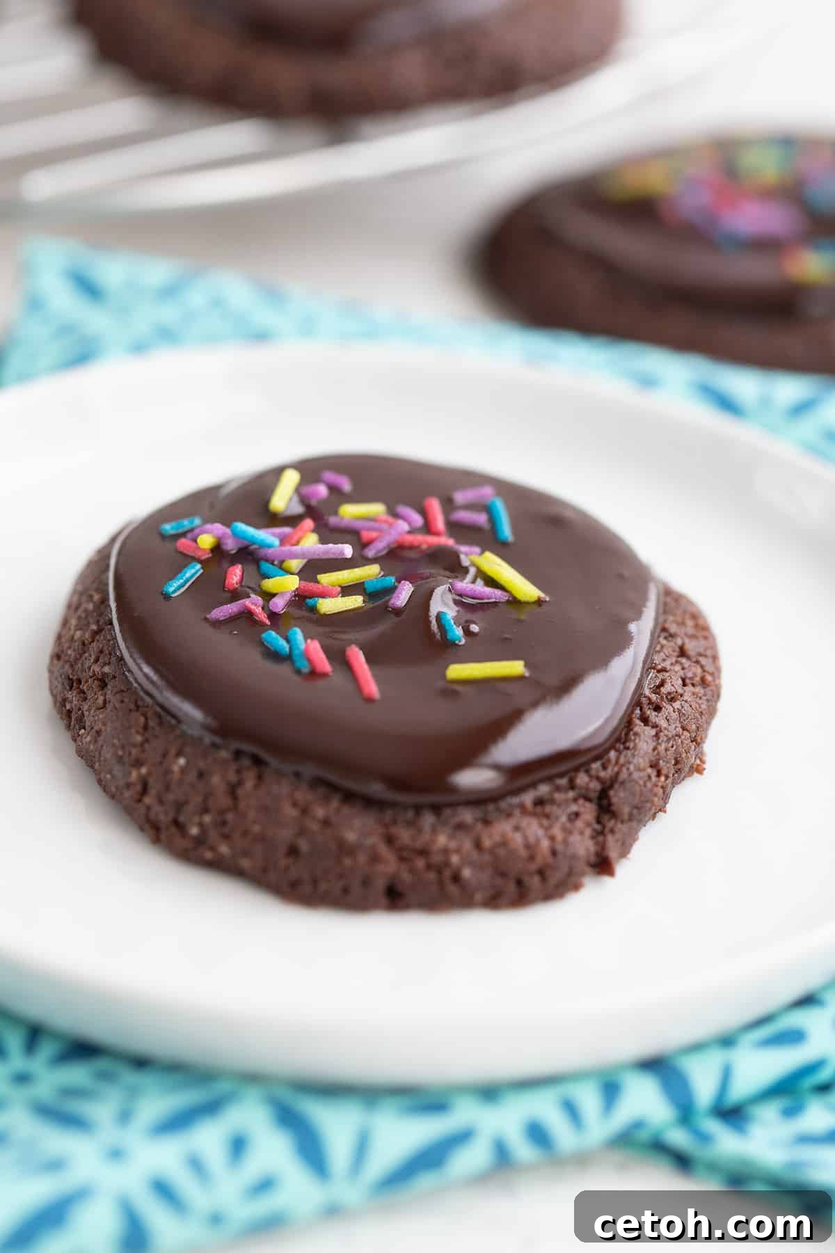 Decadent Keto Cherry Chocolate Chunk Cookies 10 Close up of a keto brownie cookie on a white plate, over a colorful teal napkin.