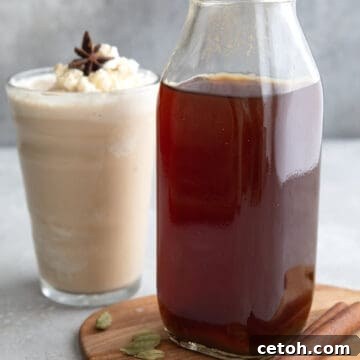 A bottle of Sugar Free Chai Concentrate on a wooden cutting board with a chai Frappuccino in the background.