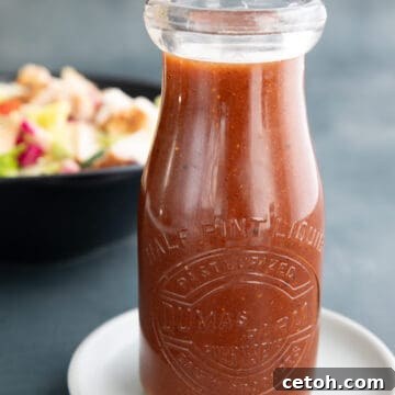 A jar of sugar free French dressing on a white plate, in front of a bowl of salad.