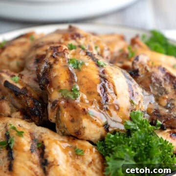 Close up shot of grilled Honey Mustard Chicken Thighs on a white plate with parsley.