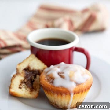Two Cinnamon Roll Protein Muffins with a cup of coffee on a white plate.