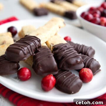 Keto Cranberry Orange Shortbread with ends dipped in chocolate piled up on a white plate over a red plaid napkin.