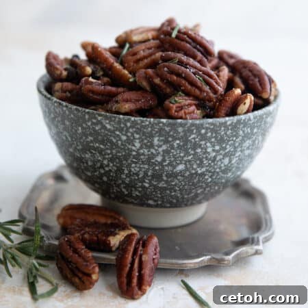Salted pecans with rosemary piled up in a speckled gray bowl on a pewter plate.
