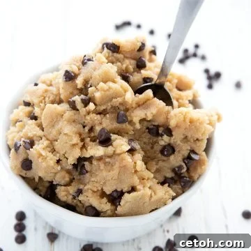 Effortless Keto Cookie Dough 2 Edible keto cookie dough piled in a white bowl with a small spoon, and chocolate chips strewn around.