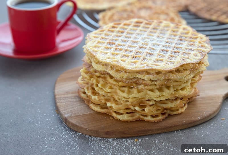 A beautifully arranged stack of keto pizzelle cookies on a rustic wooden cutting board, with a steaming cup of espresso gently blurred in the background, creating an inviting scene.