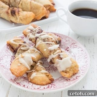 Keto Cinnamon Spirals 2 Keto cinnamon twists on a red patterned plate on a white wooden table. A cup of coffee and more cinnamon twists in the background.