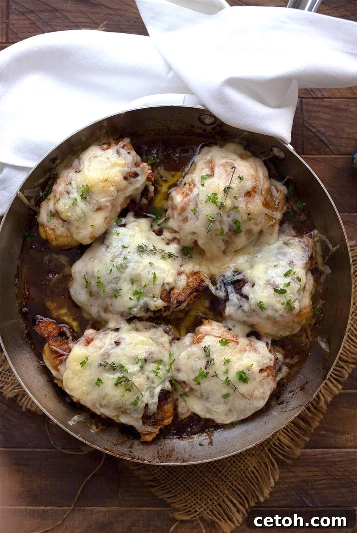 Top-down image of savory French Onion Chicken cooking in a stainless steel skillet on a rustic wooden table.