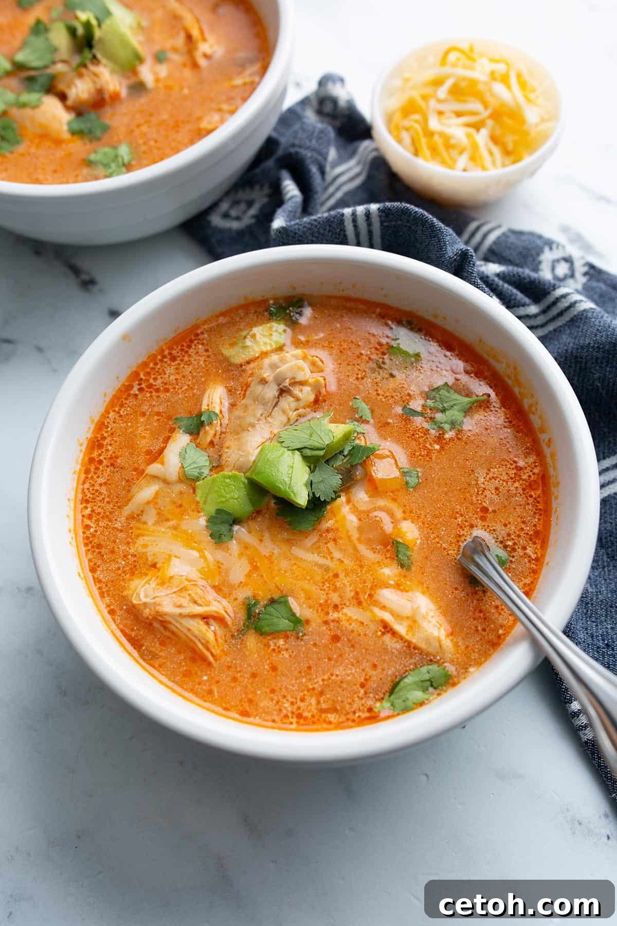 A deep bowl of hearty chicken enchilada soup with a spoon resting in it, ready to be enjoyed.