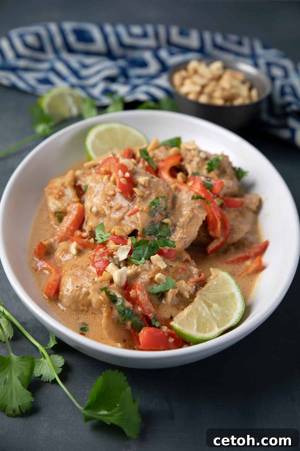 Slow Cooker Peanut Chicken beautifully presented in a white serving dish on a vibrant blue table, with scattered peanuts in the background.