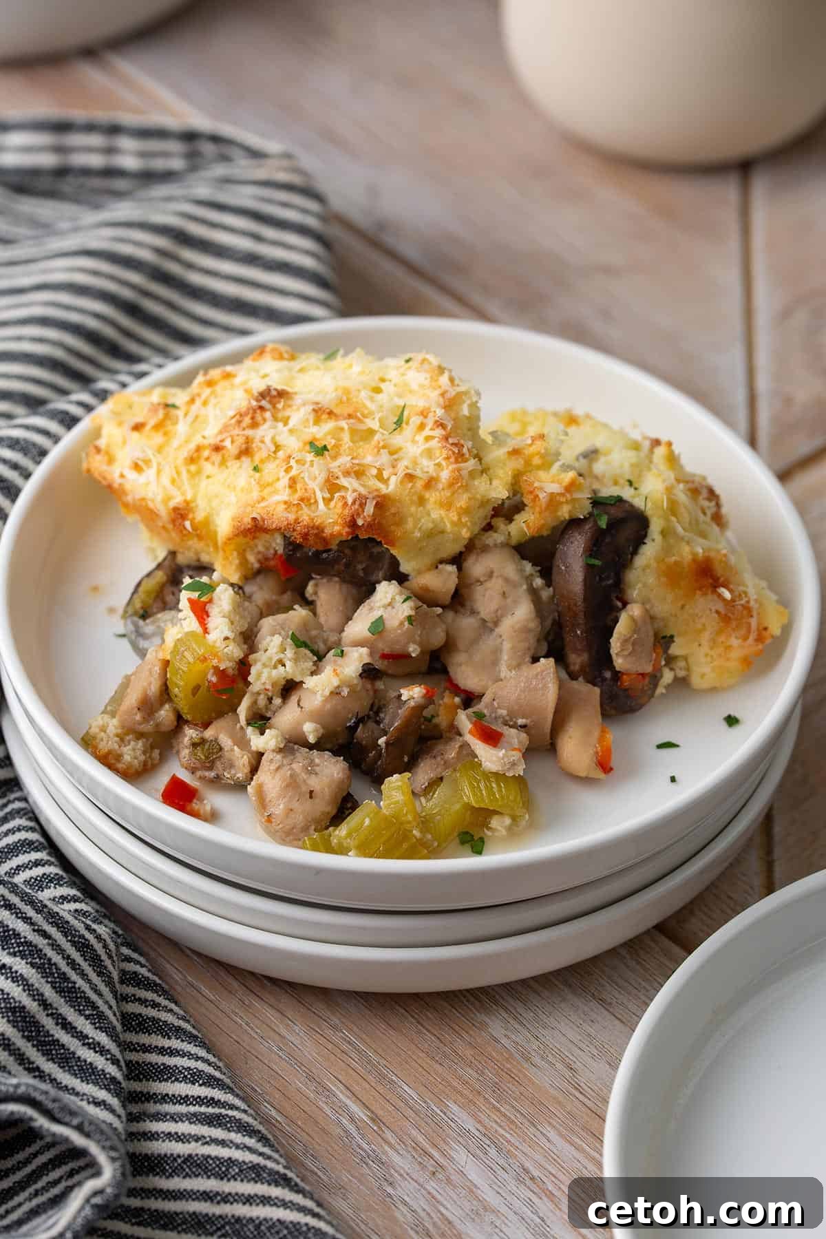 A white plate featuring a perfectly portioned serving of Keto Chicken Pot Pie, complete with a golden biscuit topping.