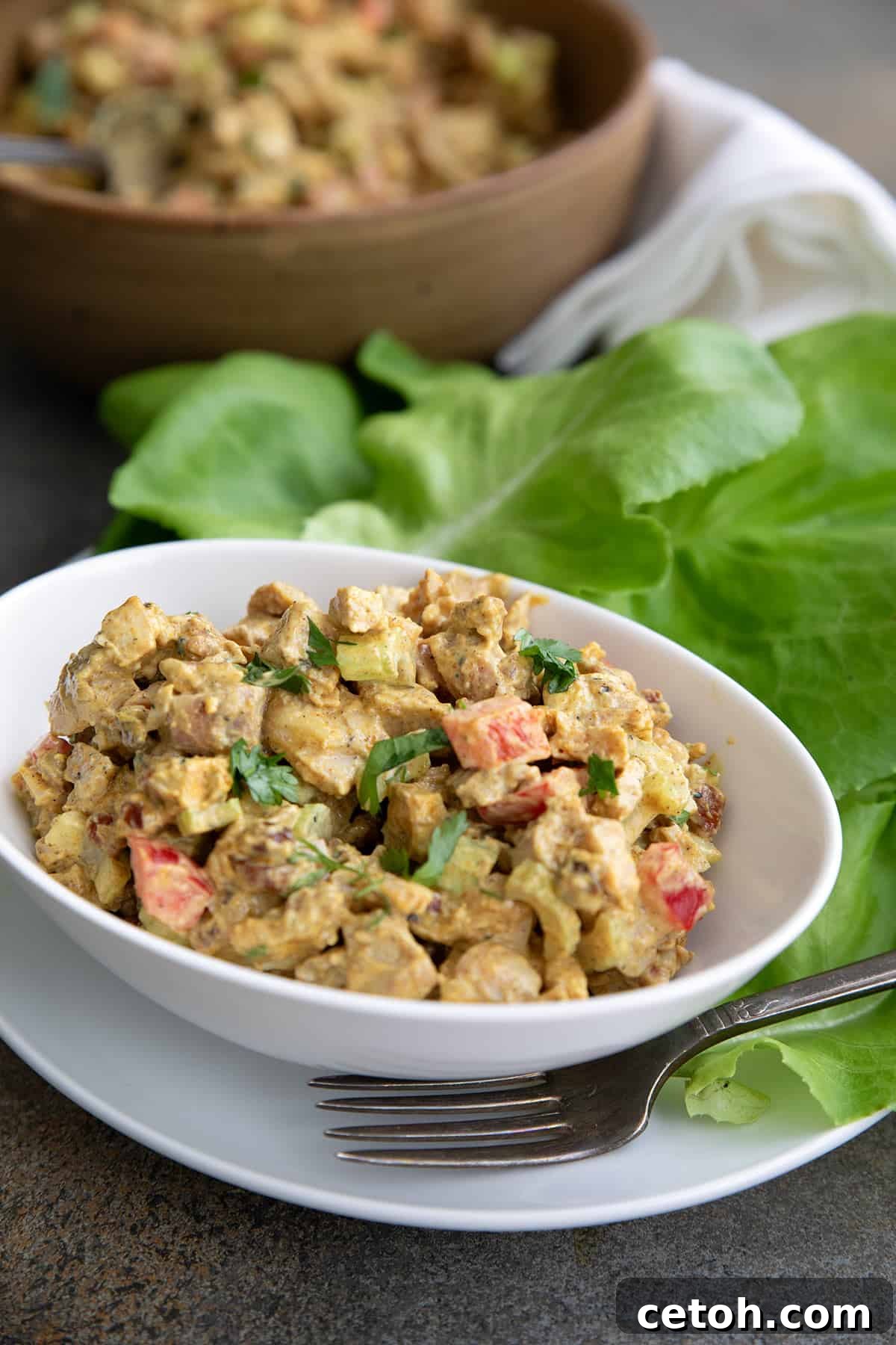 Creamy curried chicken salad artfully arranged in a white bowl, elegantly surrounded by fresh lettuce leaves.