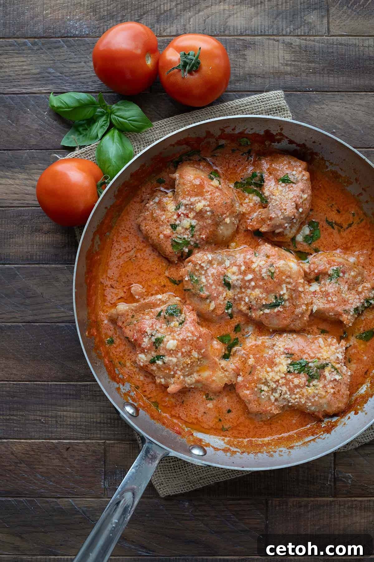 Top-down image of delicious Tomato Basil Chicken in a skillet on a rustic brown wooden table, ready to be served.