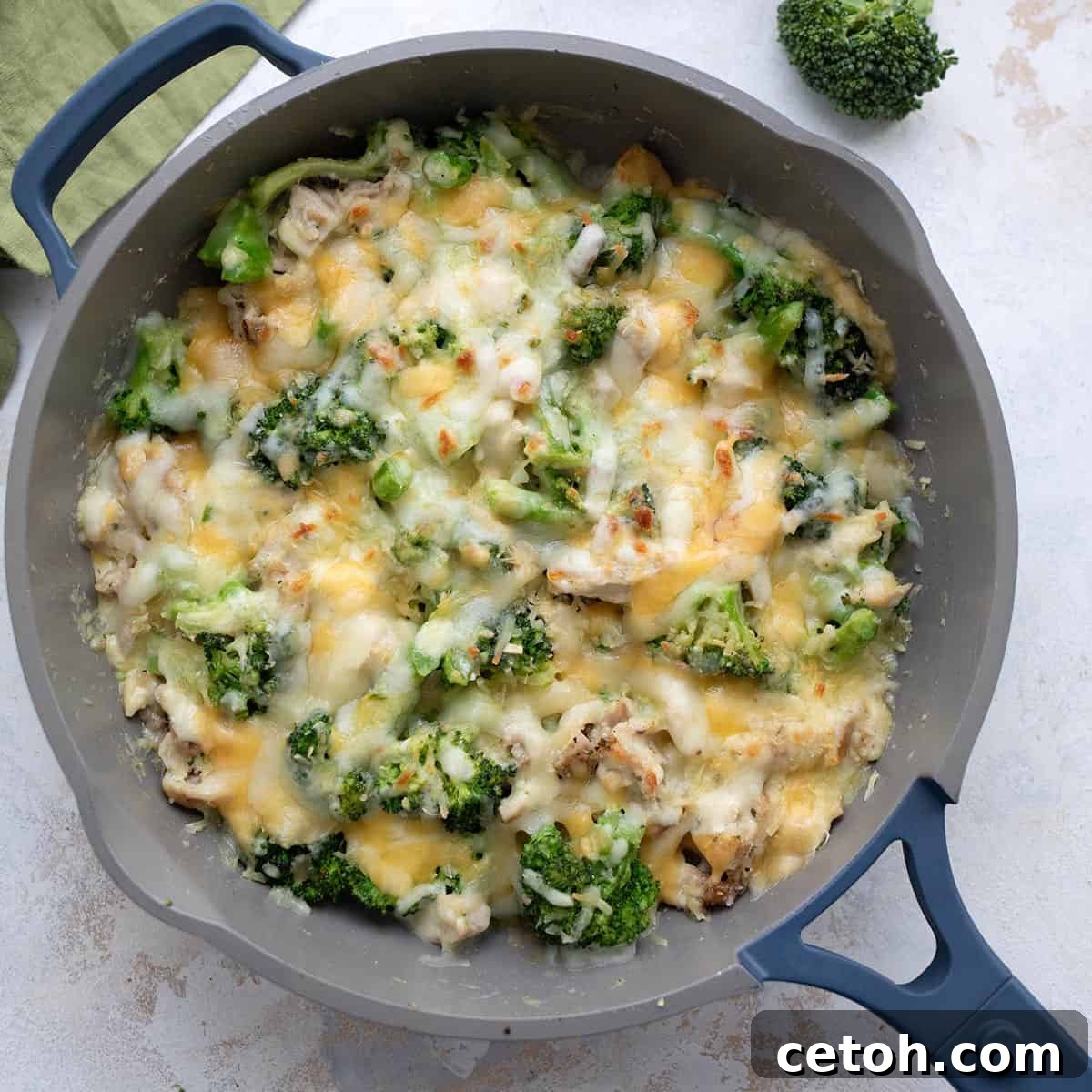 Top-down view of a bubbling cheesy Chicken Broccoli Casserole in a skillet on a white table, ready to be served.