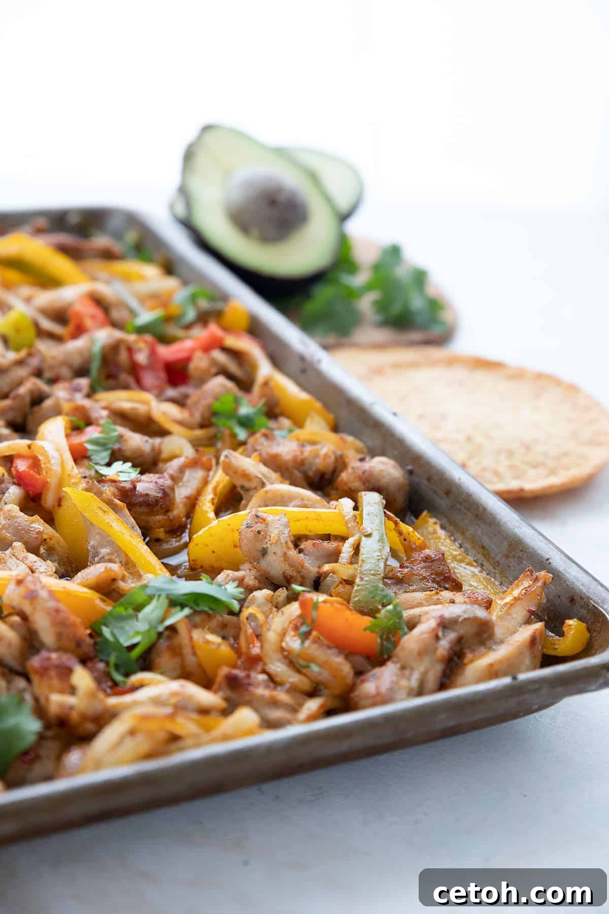 Vibrant keto chicken fajitas spread out on a sheet pan, with fresh avocado and cilantro garnishes blurred in the background.