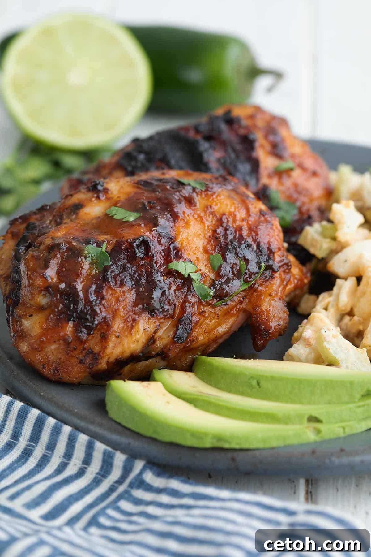 A close-up shot of a grilled chipotle lime chicken thigh on a gray plate, with fresh lime wedges and sliced jalapeño in the background.