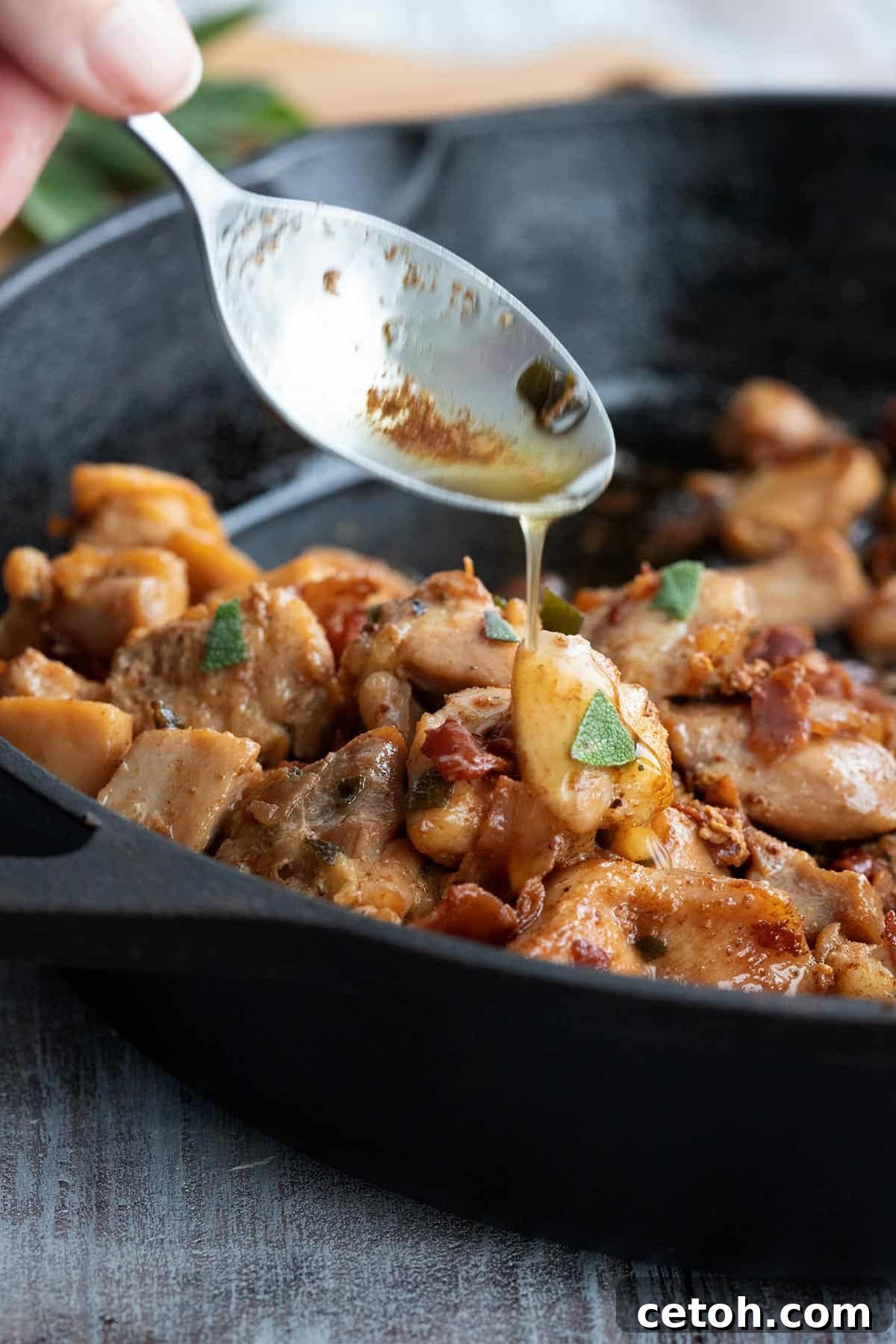 A spoon expertly pouring rich brown butter sauce over perfectly cooked chicken in a rustic cast iron skillet.