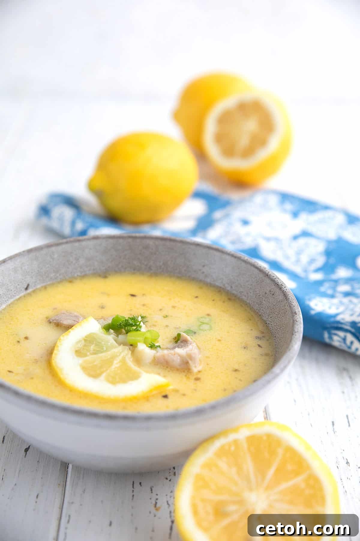 A comforting bowl of traditional Greek Lemon Chicken Soup (Avgolemono), garnished with fresh lemons and accompanied by a charming blue napkin.
