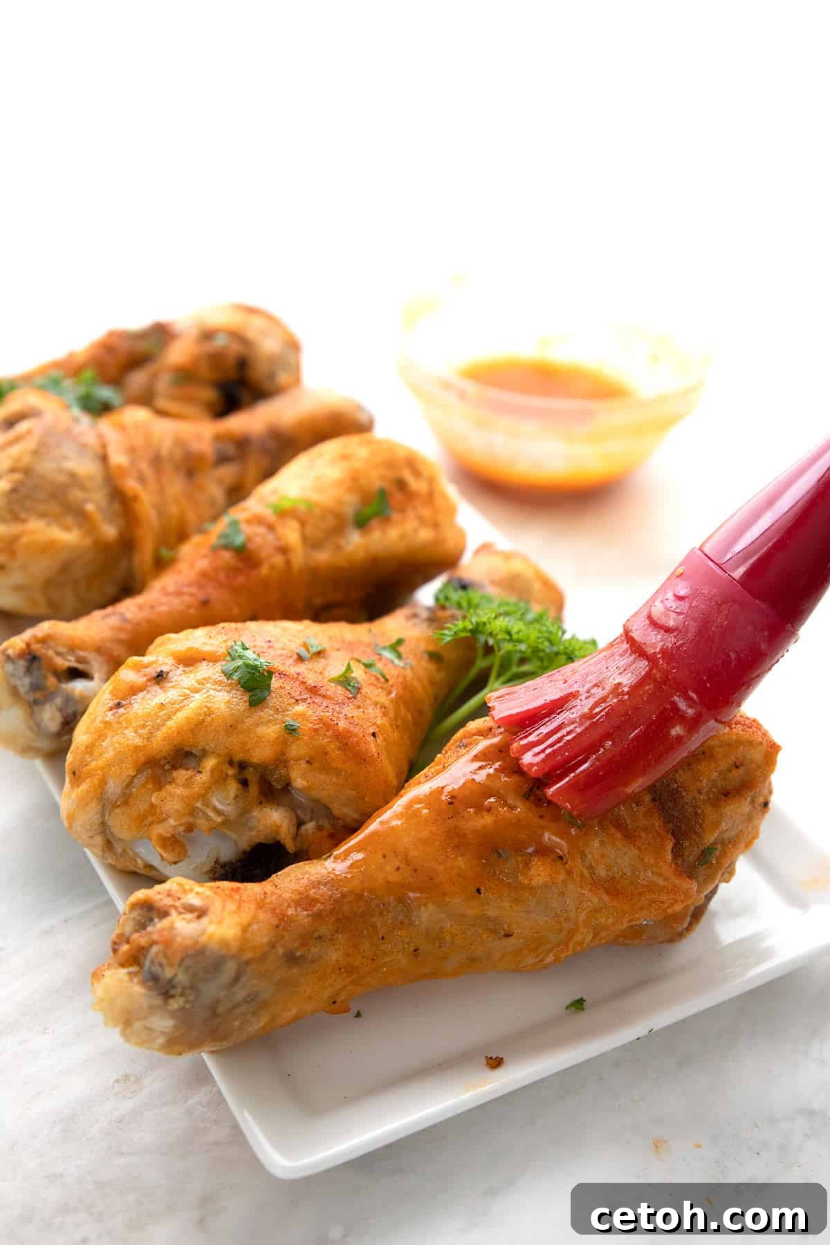 A pastry brush applies glossy Buffalo sauce over golden-brown pieces of Keto Baked Buffalo Chicken, enhancing their flavor.