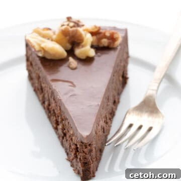 A slice of rich chocolate walnut torte on a white plate with a fork.