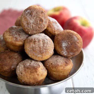 Keto Apple Cider Donut Bites stacked up on a metal cake stand on a white wooden table.