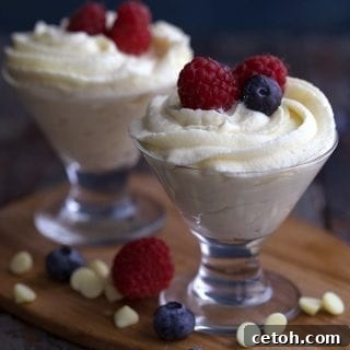 Decadent Keto White Chocolate Mousse 2 Two glass dessert cups filled with keto white chocolate mousse and fresh berries, sitting on a wooden cutting board.