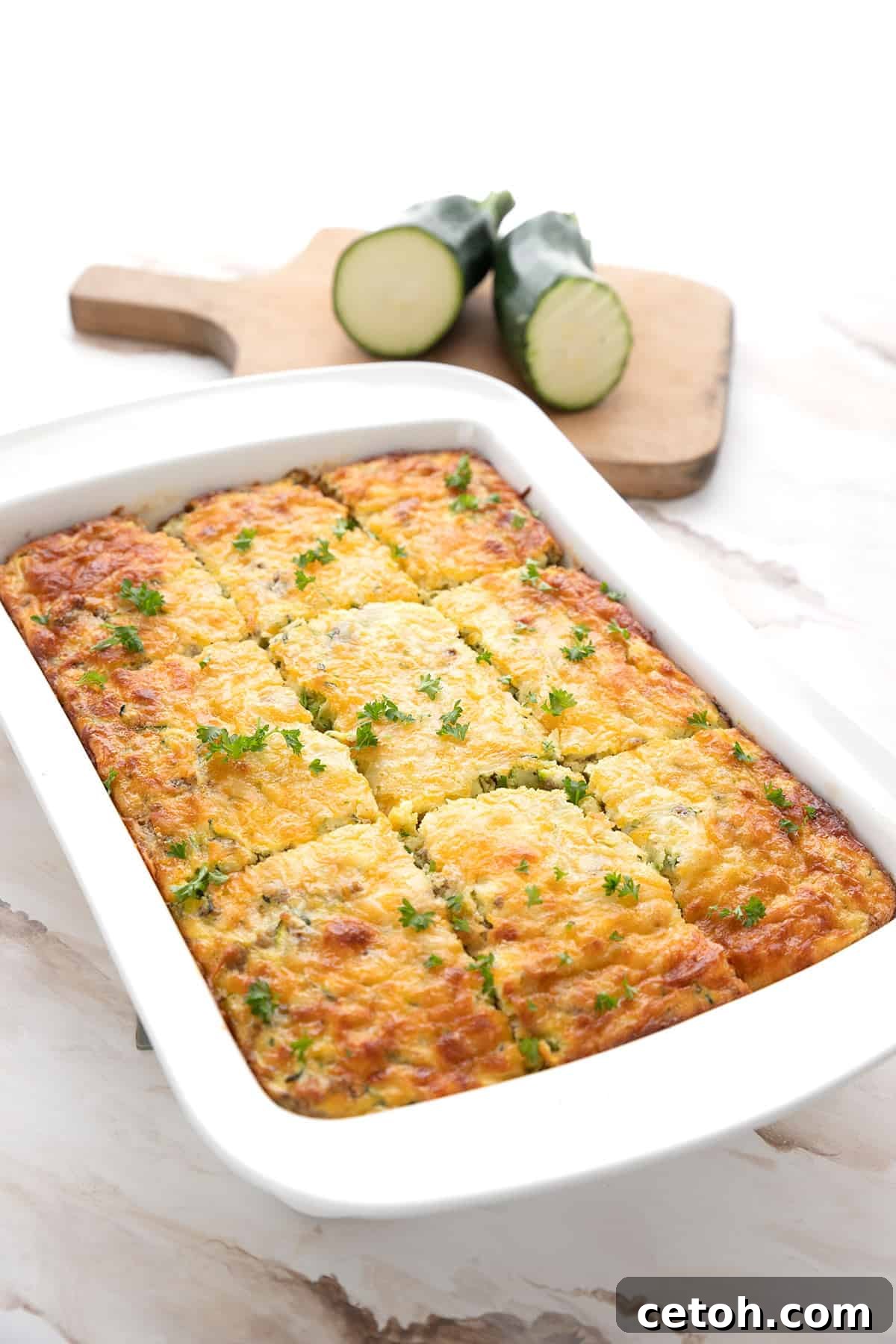 Keto Zucchini Breakfast Casserole in a white baking dish, with zucchini the background.