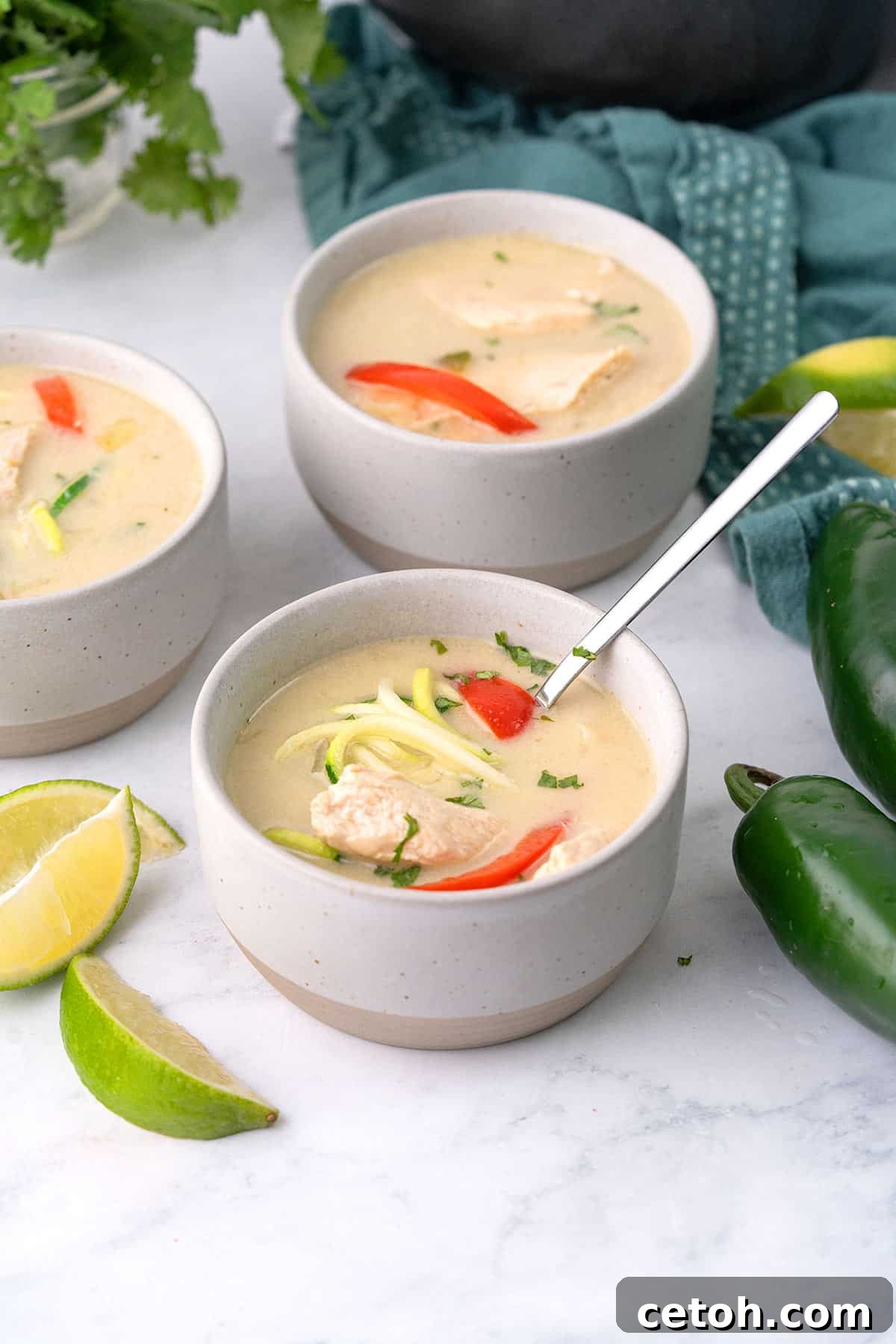 Three bowls of Keto Thai Chicken Soup on a white marble tabletop.
