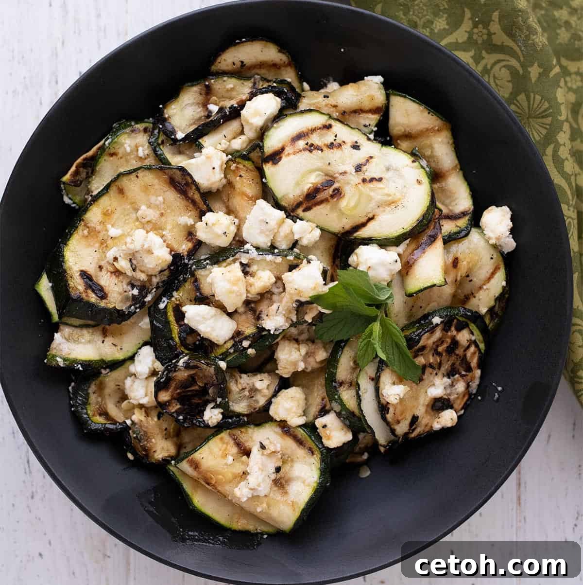 Top down image of perfectly grilled zucchini in a black bowl, topped with feta.