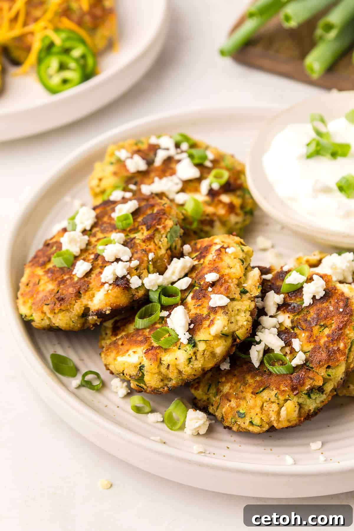 Keto Zucchini Fritters on a white plate, topped with feta and green onion.
